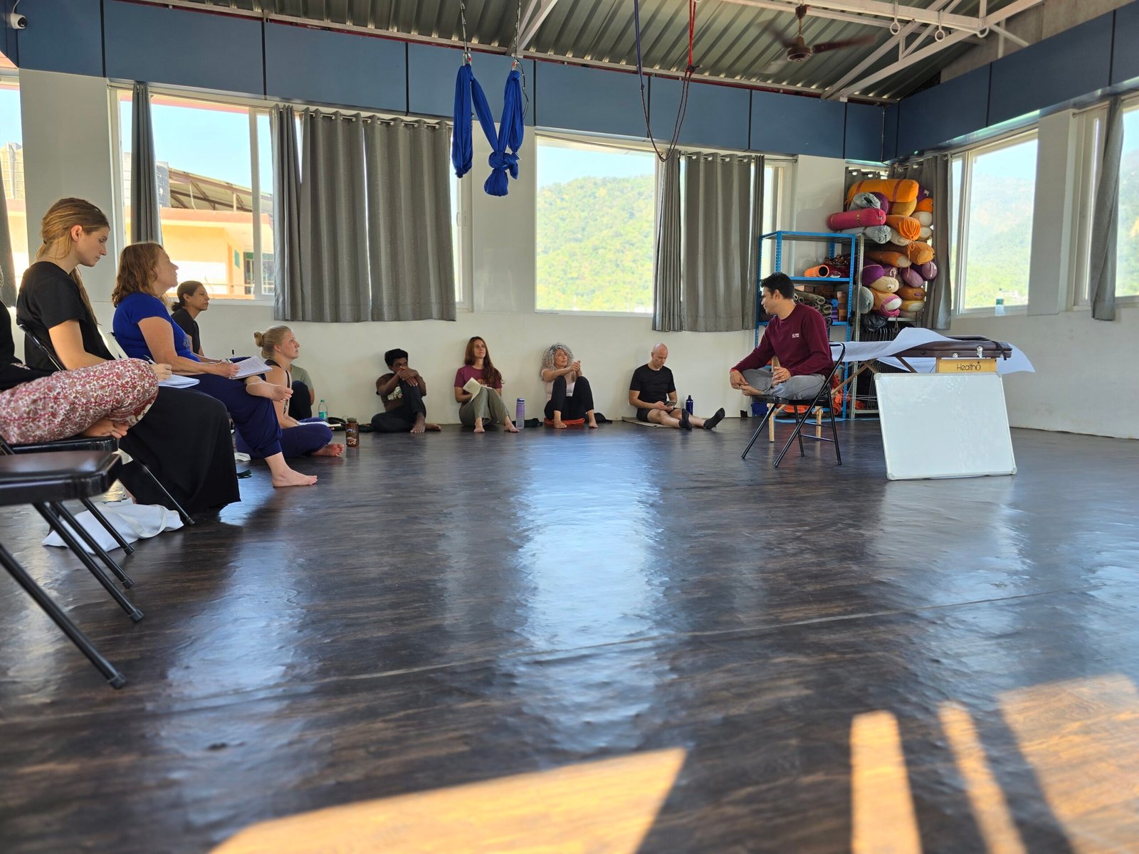Home - New Design (Draft) 5 Yoga teacher training class with students seated in a circle during theory session in a yoga studio in Rishikesh